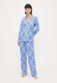 Kék és fehér mintás pizsama szett, hosszú ujjú, gombos inggel és elasztikus derékú nadrággal, paisley mintával. Puha textúra.