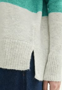 Wollmischung-Pullover mit türkisfarbenen und cremigen vertikalen Streifen, mit gerippten Bündchen und seitlichen Schlitzen am Saum. Weiche Textur, lockere Passform.