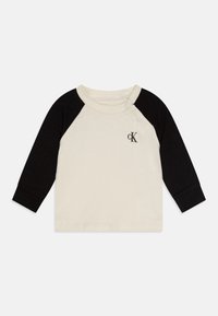 Katoenen shirt met lange mouwen, in een crèmekleurige body en zwarte raglanmouwen. Het heeft een knoop op de schouder en een klein logo op de borst.