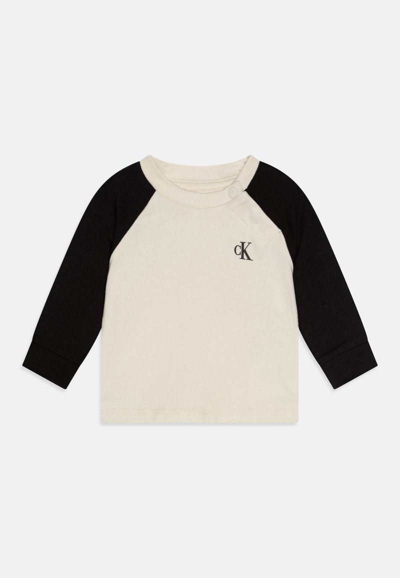 Katoenen shirt met lange mouwen, in een crèmekleurige body en zwarte raglanmouwen. Het heeft een knoop op de schouder en een klein logo op de borst.