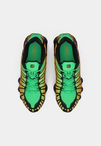 Neón zelené športové topánky s čiernymi a oranžovými akcentmi; sieťovina so zvlneným dizajnom; výnimočne polstrované podrážky a systém šnurovania.