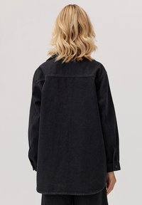 Czarna kurtka dżinsowa o luźnym kroju, z długimi rękawami i zapięciem na guzik. Gładka faktura; tył zdobi klasyczny karczek.