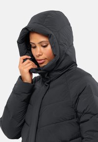 Black puffer jacket with a large hood, featuring quilted sections and a smooth texture. Adjustable front closure and hand positioning near the collar.