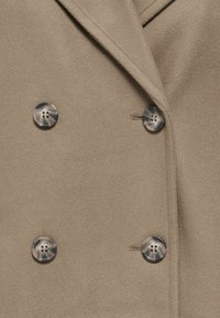 Manteau en laine beige avec revers cranté et quatre grands boutons ronds marbrés disposés en style croisé.