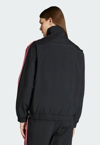 Zwarte windjack met elastische manchetten, een hoge kraag en roze zijstrepen. Lichtgewicht materiaal met een gladde textuur.