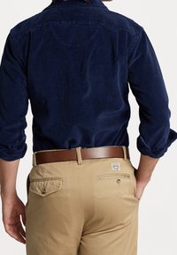 Marinblå kordflöjls skjorta med uppvikt ärm, i kombination med khakifärgade byxor. En brun läderbälte är synligt, baksidan av byxornas fickor är illustrerade.