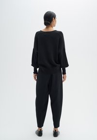 Čierny oversize sveter s padnutými plecami, textúrovaná tkanina; skombinovaný s úzkymi čiernymi nohavicami a minimalistickými čiernymi slip-on topánkami.