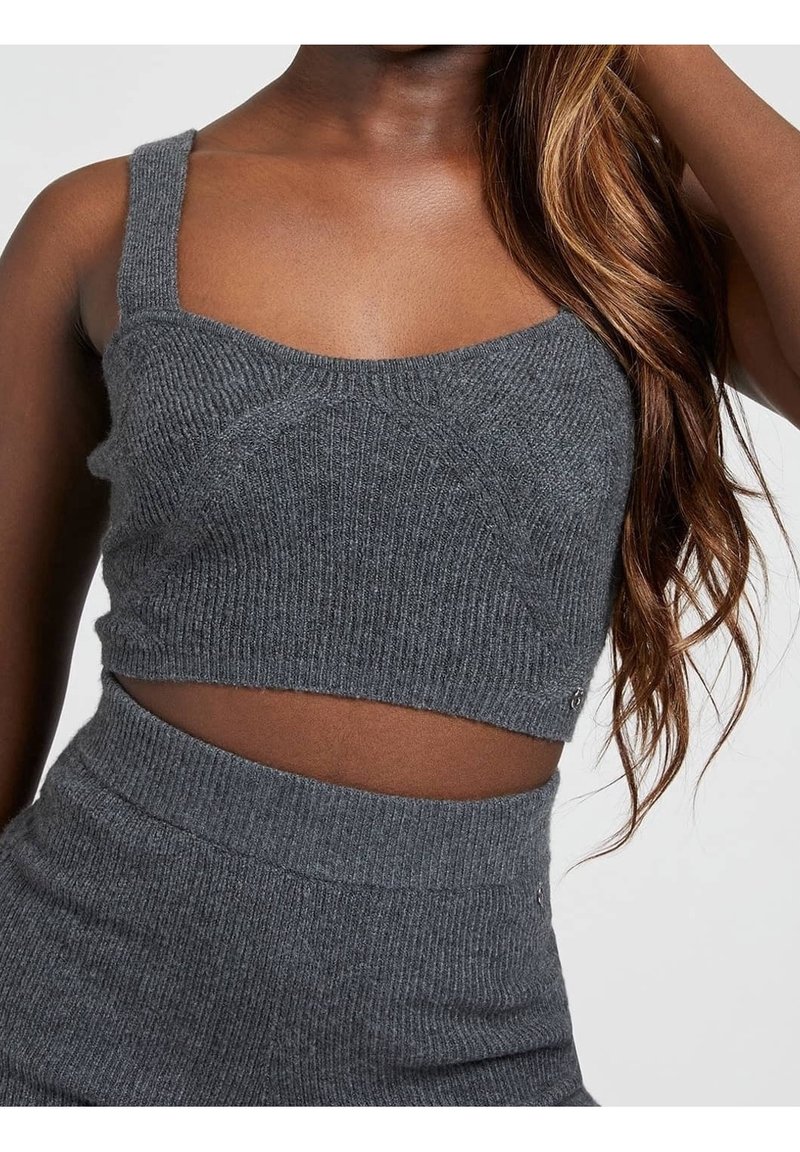 Femme portant un crop top ajusté en maille côtelée gris foncé et une jupe taille haute assortie, avec de longs cheveux ondulés tombant sur une épaule.