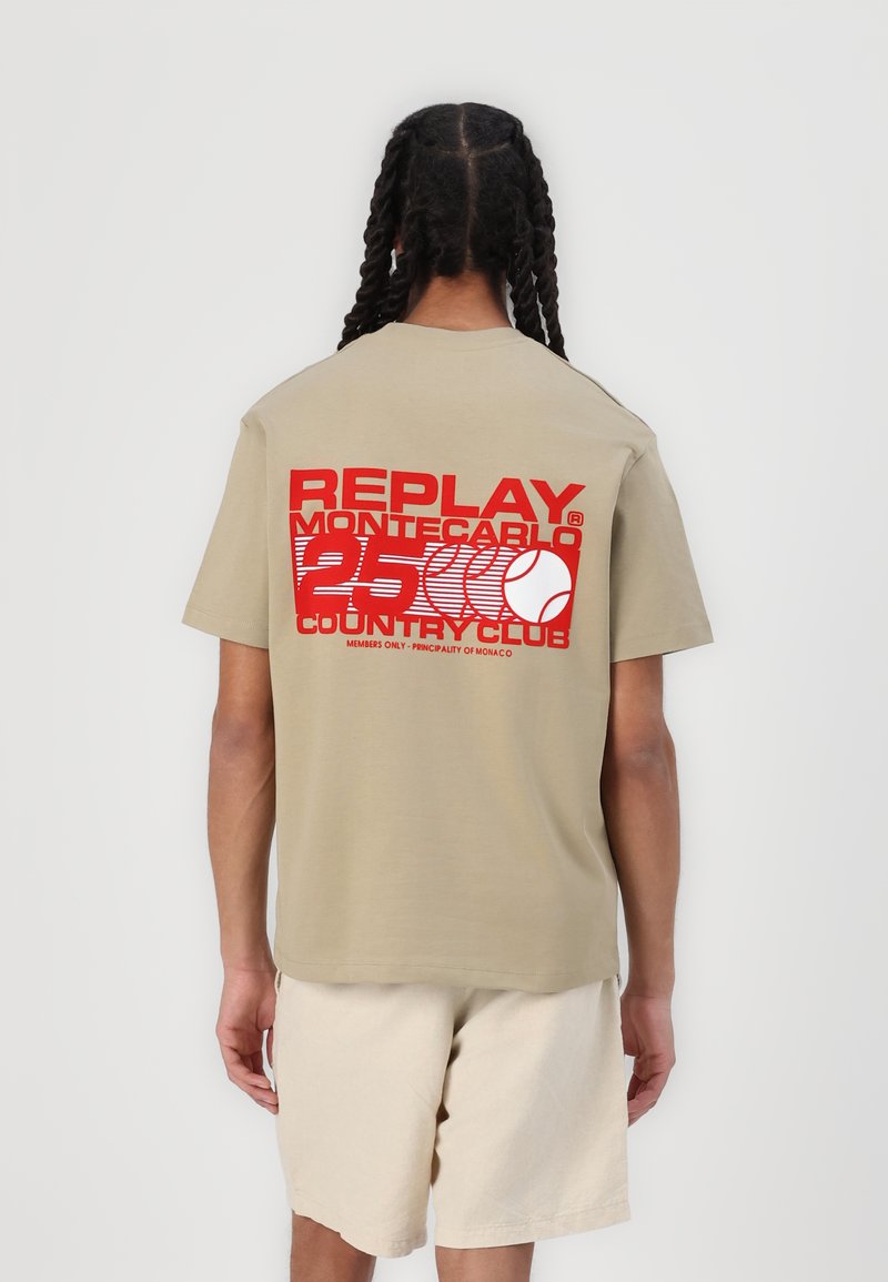 Beige bomulds t-shirt med korte ærmer og rund hals; stor rød tekst på ryggen står "REPLAY MONTECARLO 25 COUNTRY CLUB," med et grafisk design.