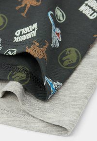 Due magliette impilate. Quella sopra è nera con grafiche di dinosauri colorate e la scritta "Jurassic World"; quella sotto è di un grigio chiaro, in tessuto testurizzato.