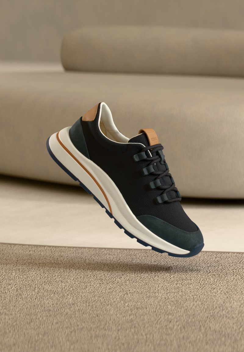 Μαύρο αθλητικό παπούτσι από διχτυωτό υλικό με υφή στη σόλα σε μπλε ναυτικό και πράσινο χρώμα, καφέ λεπτομέρεια στη φτέρνα, με επίπεδα κορδόνια και μαλακό περιμετρικό πέλμα.