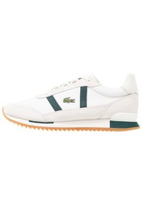 Baskets blanches avec des accents verts, en cuir et daim, avec des rayures texturées sur les côtés et une semelle extérieure en gomme imprimée.