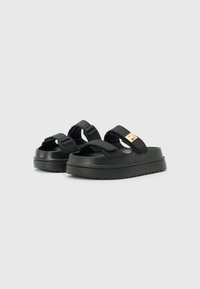 Black platform sandals with two adjustable straps, a textured upper, and a gold-toned buckle accent. Rubber sole with tread for grip.