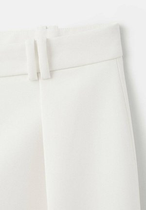 Pantalon blanc sur mesure en tissu lisse et texturé, avec une ceinture plate et deux passants décoratifs en tissu. Design minimaliste, sans poches visibles.