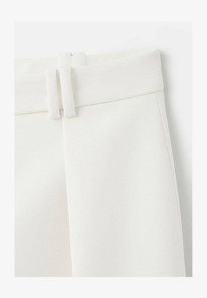 Pantalon blanc sur mesure en tissu lisse et texturé, avec une ceinture plate et deux passants décoratifs en tissu. Design minimaliste, sans poches visibles.