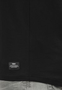 Sort T-shirt med rund hals, der har et lille figurskilt i bunden, som viser "ISOLID" og brandingdetaljer.