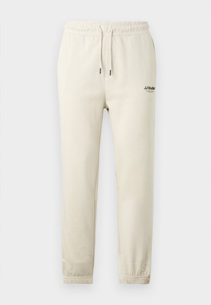 Beige joggingbroek met een elastische tailleband en boorden, met een klein zwart logo op de bovenste linkerkant van het been.