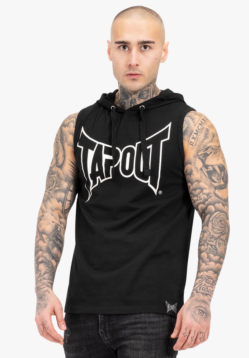 Melna bezpiedurkņu kapuce ar "TAPOUT" logo baltā krāsā, regulējams aukliņas aizdare un teksturēta auduma. Redzami ievērojami tetovējumi uz rokām.