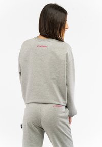 Grauer Pullover und Jogginghosen aus weichem Stoff. Mit pinken Aufschrift "ICE ICEBERG" auf dem Rücken und über der Gesäßtasche. Lockerer Schnitt.