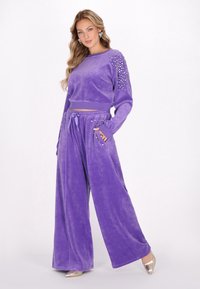 Trening din velur mov cu mâneci lungi, pantaloni evazați și decorațiuni din ținte argintii pe umeri; textură moale.