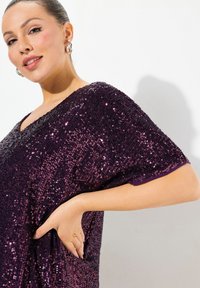 Lilla sequin-top med V-hals, flagermusærmer og loose fit. Har en skinnende tekstur og en subtil farvegradient.