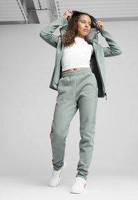 Un sweat à capuche vert clair et un jogger assorti, fabriqués en tissu doux. Le sweat à capuche a une fermeture éclair et un design sportif ; associé à des baskets blanches.