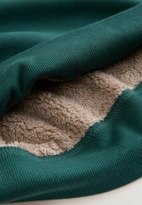 Green ribbed fabric with a beige, plush interior. The texture contrasts between smooth and soft, showcasing layered construction.