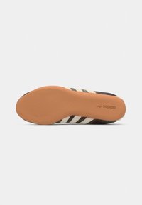 Sole di scarpa nera e crema con texture distintiva; presenta tre accenti a strisce e una suola in gomma tan con dettaglio del logo.