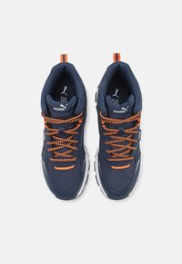 Baskets navy avec des accents orange, dotées de cols rembourrés, de lacets texturés et de semelles blanches. Logo de la marque sur la languette et le côté.