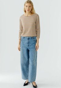 Gestreepte lange mouwen top in bruin en crèmekleur, gecombineerd met een lichtblauwe wijde broek. De outfit heeft een knoopdetail op de schouder.