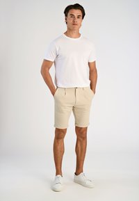 White cotton t-shirt, beige tailored shorts with rolled cuffs, and white sneakers. Simple design, smooth texture, casual fit.