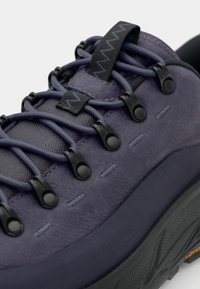 Zapato de senderismo púrpura con parte superior texturizada, acentos de hardware negro y cordones elásticos. Cuenta con una suela resistente para una tracción mejorada.