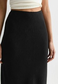 Gonna nera a vita alta realizzata in tessuto texturizzato, con una finitura liscia e una silhouette dritta; presenta una cintura sopra un taglio aderente.