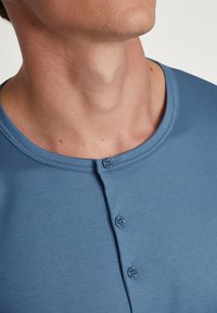 Blauwe katoenen henley shirt met een ronde hals, drie knopen en korte mouwen. Gladde textuur met een subtiel heidepatroon.