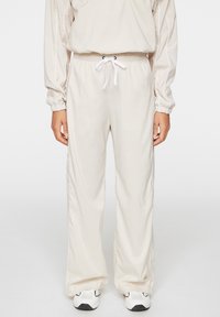 Beiga träningsbyxor med elastisk midja och dragsko, med sidostripes och en lös, rak ben-design.