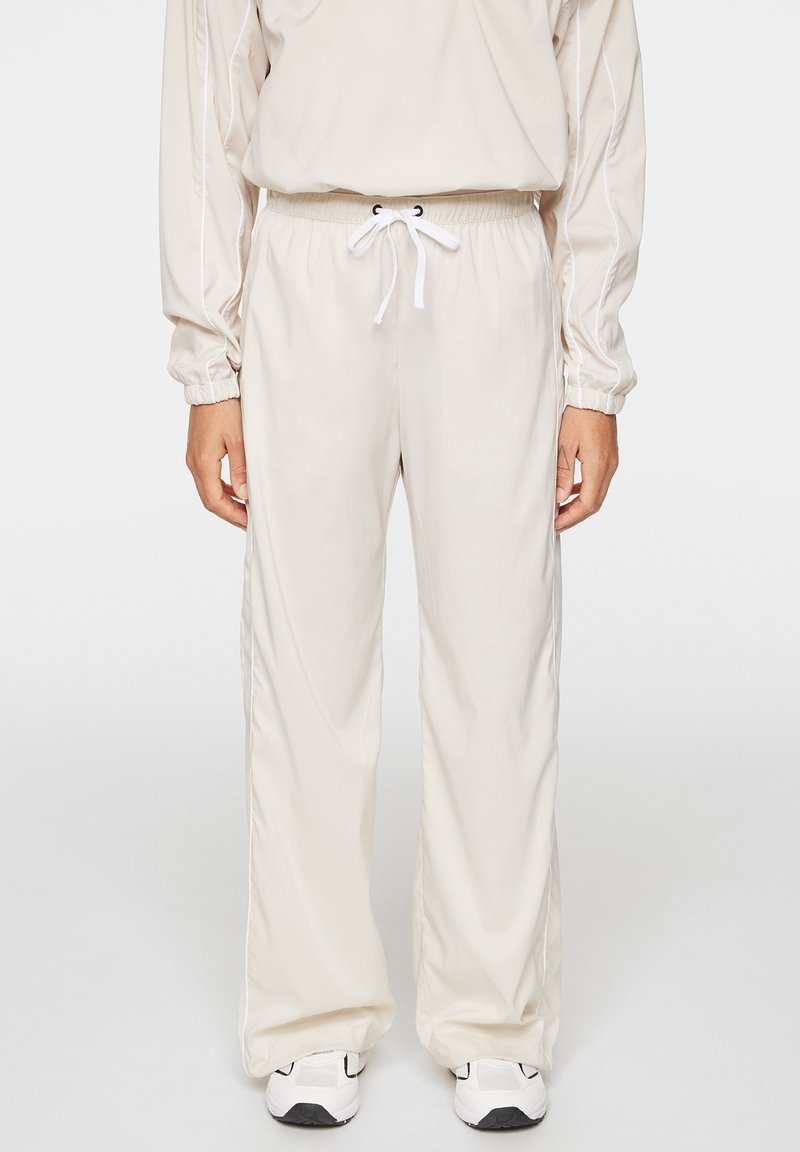 Beiga träningsbyxor med elastisk midja och dragsko, med sidostripes och en lös, rak ben-design.