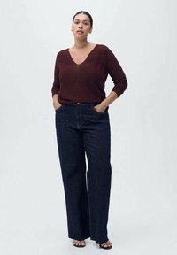 Bordeaux sweter w serek z długimi rękawami, zestawiony z ciemnoniebieskimi spodniami z szerokimi nogawkami, charakteryzującymi się klasycznym designem dżinsu i minimalnymi detalami metalowymi.