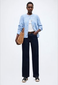 Ανοιχτό μπλε πλεκτό πουλόβερ, λευκό τοπ, σκούρο τζην παντελόνι με φαρδύ πόδι, καφέ ζώνη, καφέ τσάντα, μαύρα και λευκά αθλητικά παπούτσια.