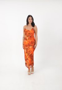 Orange blomstermønstret, ærmeløs maxi kjole i let stof. Designet har store, abstrakte bladformer i nuancer af orange og brun.