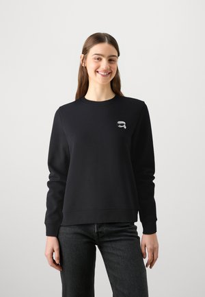 Black sweatshirt made from soft fabric with long sleeves, crew neckline, and a small graphic on the chest. Worn with dark jeans.