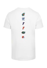 T-shirt alb din bumbac cu cinci modele de logo-uri aliniate vertical pe spate, inclusiv un aligator, text și o cască de fotbal.