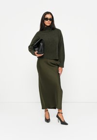 Oliven grønn strikkegenser med høy hals, parret med en silkeaktig oliven grønn maksikjole. Svart clutch og hæler fullfører antrekket.