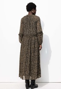 Robe longue noire à fleurs avec des manches longues et fluides, un corsage ajusté froncé à la taille, et une jupe fluide. Des bottines noires à la cheville complètent le look.