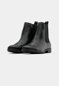 Schwarze Leder ankle boots mit elastischen Seitenteilen und Ziehschlaufen, niedrigen Blockabsätzen, vor einem weißen Hintergrund präsentiert.