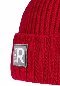 Red knitted beanie with a ribbed texture, featuring a gray rectangular patch labeled “#1839” and a white "R" in the center.