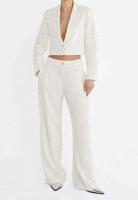 Blazer blanc raccourci avec un seul bouton et manches longues, associé à un pantalon blanc à jambes larges. Le tissu présente une texture légère. Chaussures pointues argentées.