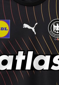 Zwarte sporttrui met oranje strepen, voorzien van een wit Puma-logo, een ronde badge met een dubbelhoofdige adelaar en grote letters "atlas."