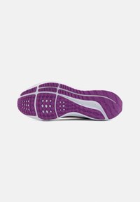 Semelle de chaussure avec bande de roulement en caoutchouc violet, semelle intermédiaire blanche et motifs d’adhérence pour la traction, vue par dessous sur fond blanc.