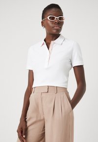 Polo bianco con colletto rosa pallido, maniche corte e chiusura a bottoni. Abbinato a pantaloni beige chiaro a vita alta.