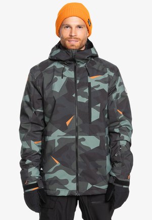 Chaqueta de camuflaje en verde y negro con acentos naranjas, que presenta un cierre frontal, capucha y puños ajustables. Tejido suave y texturizado.